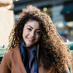 Woman with curly hair wearing a brown coat in an urban setting